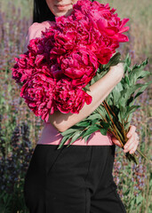 Brunette in a field with a bouquet of burgundy peonies. 
