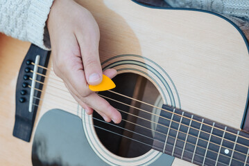 Hand of a girl, holding orange mediator in her hand and playing the guitar, close up. Concept of...