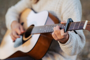 Guitar in hands of a young woman playing it. Playing music outdoors, using equipment capo