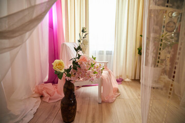 Delicate bright pink interior of the room with armchair, a vase with roses, draped curtains and a window. Location and background in the photo studio
