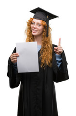 Young redhead woman wearing graduate uniform holding degree surprised with an idea or question pointing finger with happy face, number one