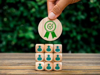 Eco friendly business goal and success, approved, winner, teamwork and company concept. Award icon on top of wooden cube block with person symbol on blocks pyramid shape on green leaves background.