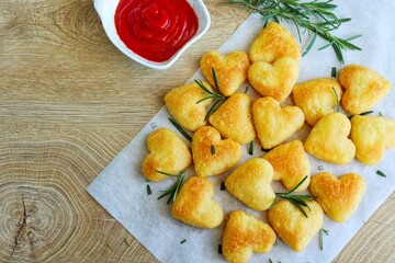 Roasted heart shape mashed potatoes with rosemary served with ketchup on parchment paper with wooden table background.Healthy vegetarian concept  for celebrate Valentine's day.Top view with copy space