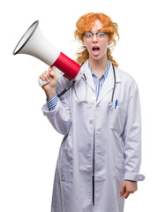 Young redhead doctor woman holding megaphone scared in shock with a surprise face, afraid and excited with fear expression