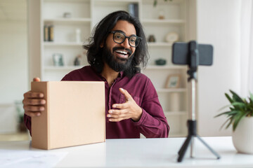 Indian influencer guy wearing glasses making video review of product at camera - obrazy, fototapety, plakaty