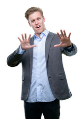 Young handsome blond business man afraid and terrified with fear expression stop gesture with hands, shouting in shock. Panic concept.