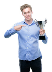 Young handsome blond man holding a trophy very happy pointing with hand and finger