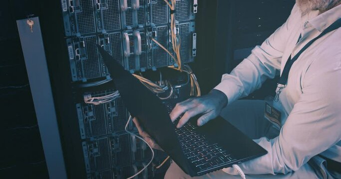 Man in data center with laptop, typing and network maintenance with engineer in digital storage for update. Tech employee, system administration and technician online in server room with computer.