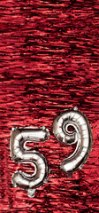 Silver foil balloon number number 59 on a background of red tinsel decoration. Birthday greeting...