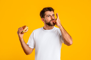 Portrait Of Smiling Hungry Man Eating Burger Licking Fingers, Studio