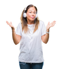 Middle age hispanic woman listening to music wearing headphones over isolated background clueless and confused expression with arms and hands raised. Doubt concept.