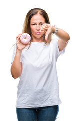 Middle age hispanic woman eating pink donut over isolated background with angry face, negative sign showing dislike with thumbs down, rejection concept