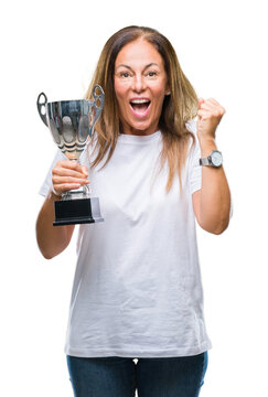 Middle age hispanic winner woman celebrating award holding trophy over isolated background screaming proud and celebrating victory and success very excited, cheering emotion