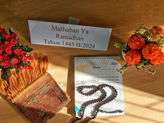 monthly calendar for 2024, writing welcoming the month of Ramadan, as well as prayer beads and prayer mats with two flowers in a small pot
