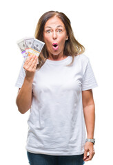 Middle age hispanic woman holding bunch of dollars over isolated background scared in shock with a surprise face, afraid and excited with fear expression