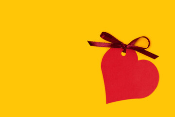 Red empty tag in a heart shape with tied ribbon bow on a yellow background.