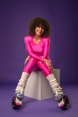 Sporty woman with curly hair in pink tracksuit wearing sports shoes kangoo jumpers posing in studio on background