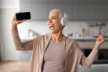 senior woman with headset and phone dancing and singing indoor