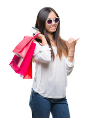 Young asian woman holding shopping bags on sales over isolated background pointing and showing with thumb up to the side with happy face smiling