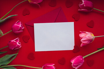 Empty white envelope copy space for your text or design with beautiful pink tulip bouquet on red background. Red small heart. Love romance Valentines day. Template mock up for holiday spring greeting