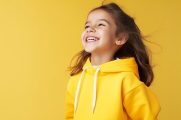 Portrait of a smiling little girl in yellow hoodie over yellow background
