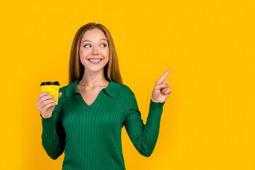 Portrait of young girl student holding tasty coffee direct finger empty space interested new news isolated on yellow color background