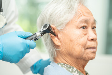Audiologist or ENT doctor use otoscope checking ear of asian senior woman patient treating hearing loss problem. - obrazy, fototapety, plakaty