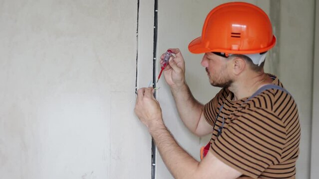 male electrician hands checks presence of electrical voltage in socket phase uses electrical tester screwdriver. Examining three coloured wires in outlet by voltage detector indoor.