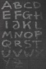 handwritten alphabet letters on dark paper material.