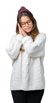 Young beautiful brunette hipster woman wearing glasses and winter hat over isolated background sleeping tired dreaming and posing with hands together while smiling with closed eyes.