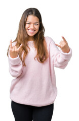 Young beautiful brunette woman wearing pink winter sweater over isolated background shouting with crazy expression doing rock symbol with hands up. Music star. Heavy concept.