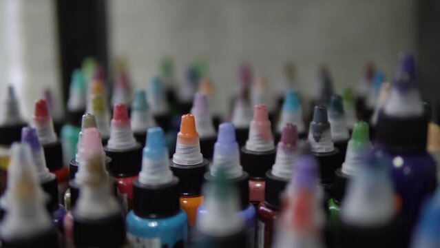 Color selection. Tubes with paints. Ink for tattoos. The girl chooses the color. All the colors of the rainbow. Bottles with colored paints. Female hand selects tubes with paint for drawing.