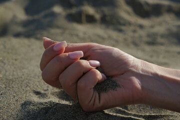 Close-up of a woman's hand releasing falling sand. Sand flows through your hand against the...