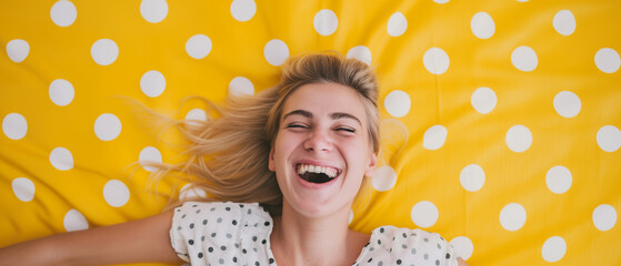 Mulher loira feliz deitada em um tapete amarelo com bolinhas brancas - obrazy, fototapety, plakaty
