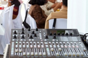 A sound mixer control panel with some people in the background wedding concepts.