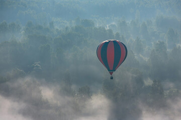 A colorful hot air balloon flies over a forest covered with fog. Early summer morning. Balloon...