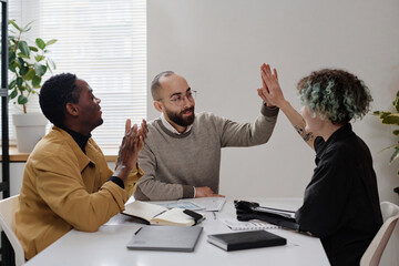 Male and female office workers giving each other high five, their black colleague applauding them