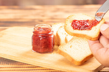 Jam and toast, hand spreading jam on toast with knife on rustic wood. Selective focus.