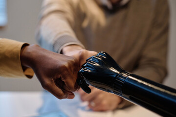 Two biracial people and person with prosthetic arm fist bumping each other - Powered by Adobe
