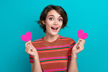 Photo of lovely good mood impressed woman dressed striped t-shirt hold two paper heart postcards isolated on turquoise color background
