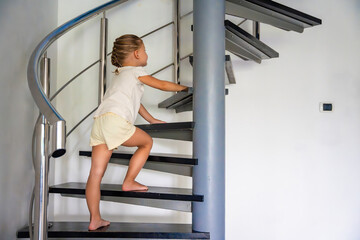 Little girl going up the stairs at home, child climbing spiral staircase. Dangerous situation at...