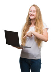 Blonde teenager woman using computer laptop very happy pointing with hand and finger