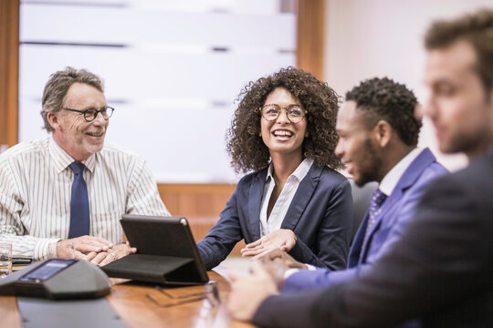 Woman of African descent in business attire and her colleagues sitting at desk having a meeting an a large office. Cape Town, South Africa