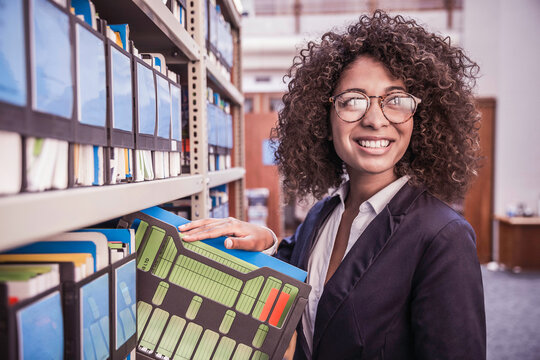 Young African corporate woman looking through shelves with binders and books in large start-up office space. Cape Town, South Africa