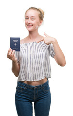 Blonde teenager woman holding passport of Germany with surprise face pointing finger to himself