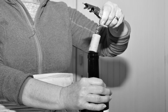 mani di donna che stappano con il cavatappi la bottiglia di vino con tappo di sughero dentro la cucina, foto in bianco e nero
