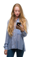 Blonde teenager woman using smartphone with a confident expression on smart face thinking serious