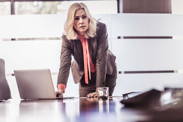 Business woman leaning over her desk and laptop while contemplating her next move.