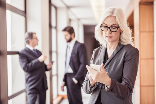 Business colleagues walking down a corridor together at the office while brainstorming and looking at smart phone. - Powered by Adobe