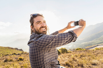 Portrait of man with beard smiling in the camera while taking selfy while hiking in the hills. Franschoek, South Africa